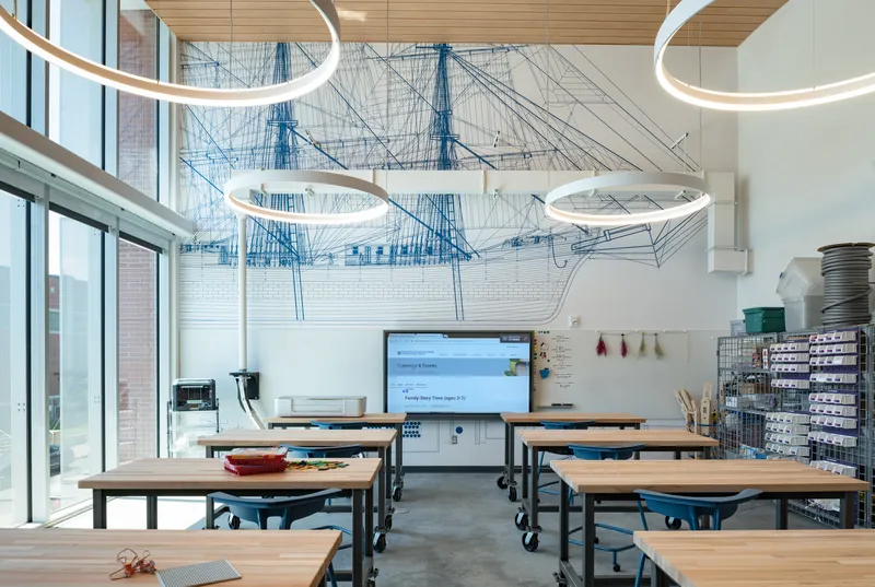 Interior view of work tables beneath a mural installation and suspended ring lighting fixtures