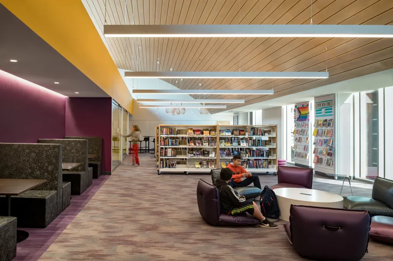 Reading area with purple upholstered seating, wood slat ceiling, and two patrons beneath skylights