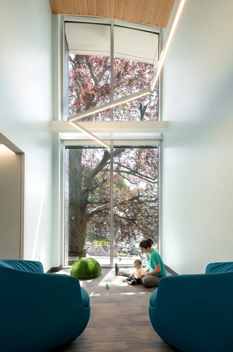 Double-height window wall framing a cherry blossom tree with mother and child seated on the floor
