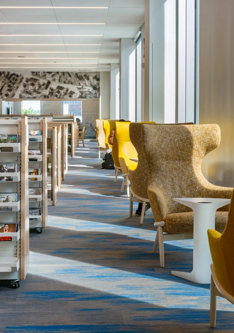 Library reading area with striped carpet, wingback chairs, and mosaic tile artwork above tall windows