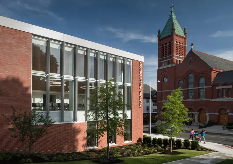 Street view of the glazed brick facade with tall windows beside the red brick church tower