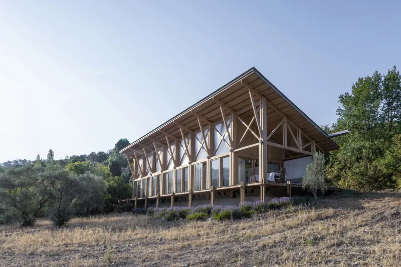 Timber-framed pavilion with exposed diagonal bracing set on a hillside among lavender and dry grass