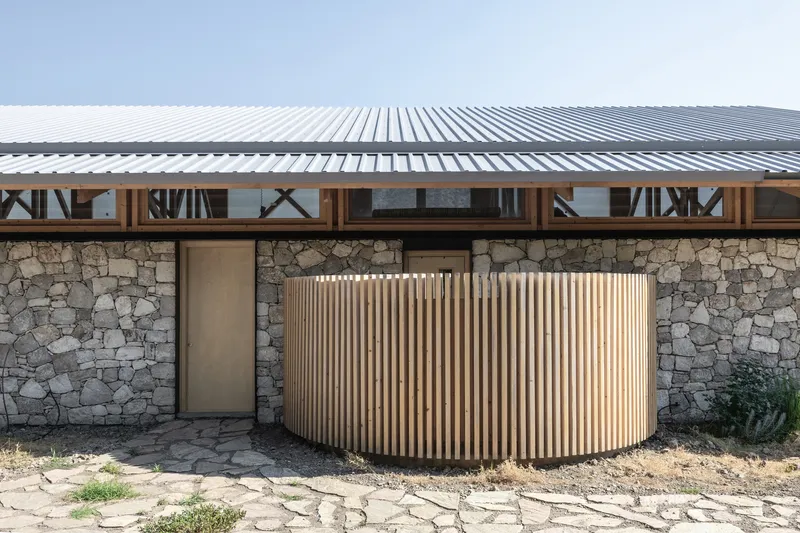 Curved timber slat screen beside a stone wall beneath a corrugated metal roof overhang