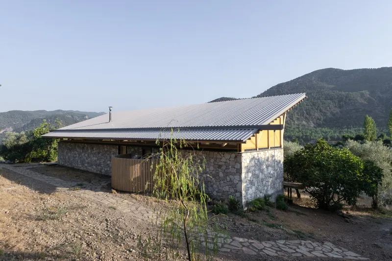 Corrugated metal roof spanning stone walls with olive trees and mountains in the background