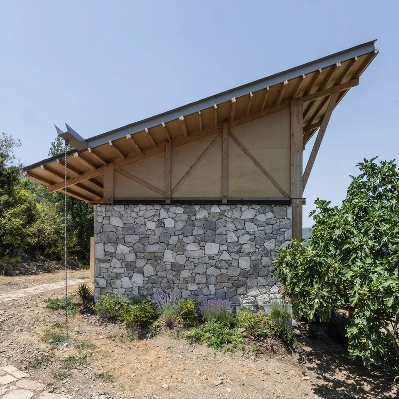 Rear gable end showing timber truss infill panels above rubble stone walls and planted beds