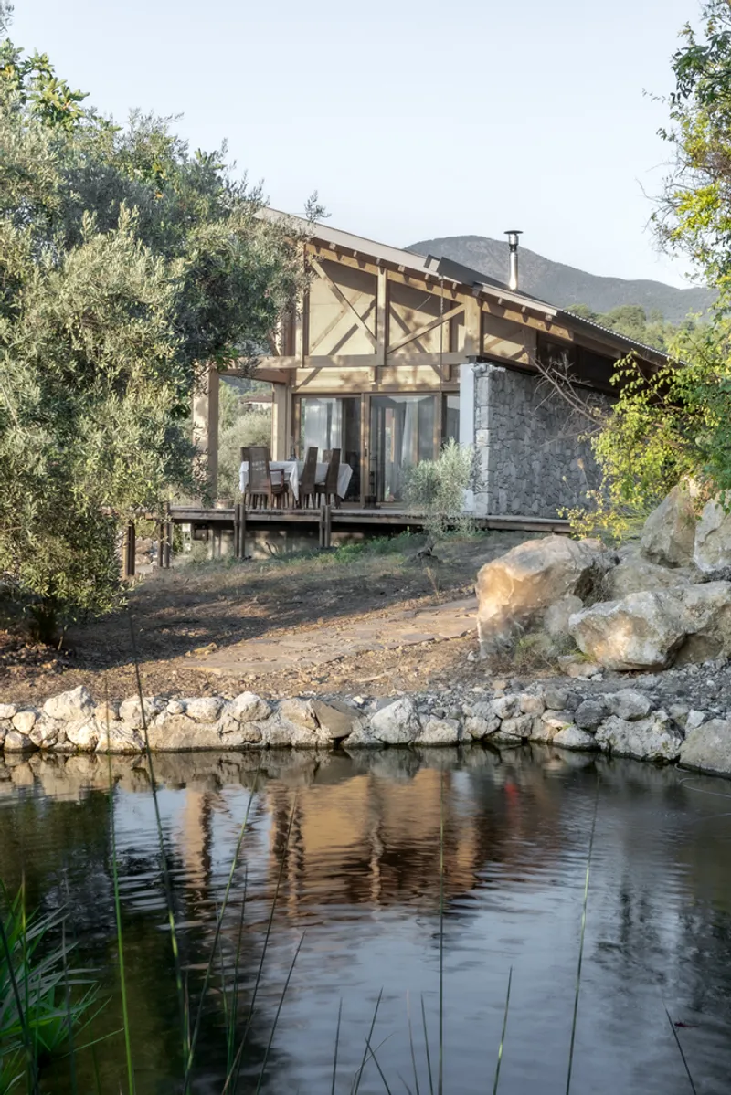 Covered timber deck and stone facade reflected in a still pond surrounded by native plantings