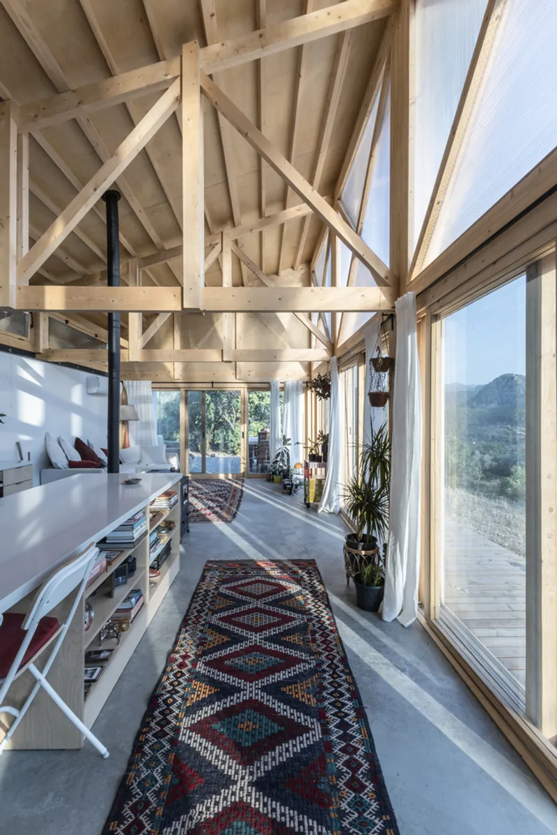 Interior view of exposed timber truss ceiling with floor-to-ceiling glazing and patterned rug