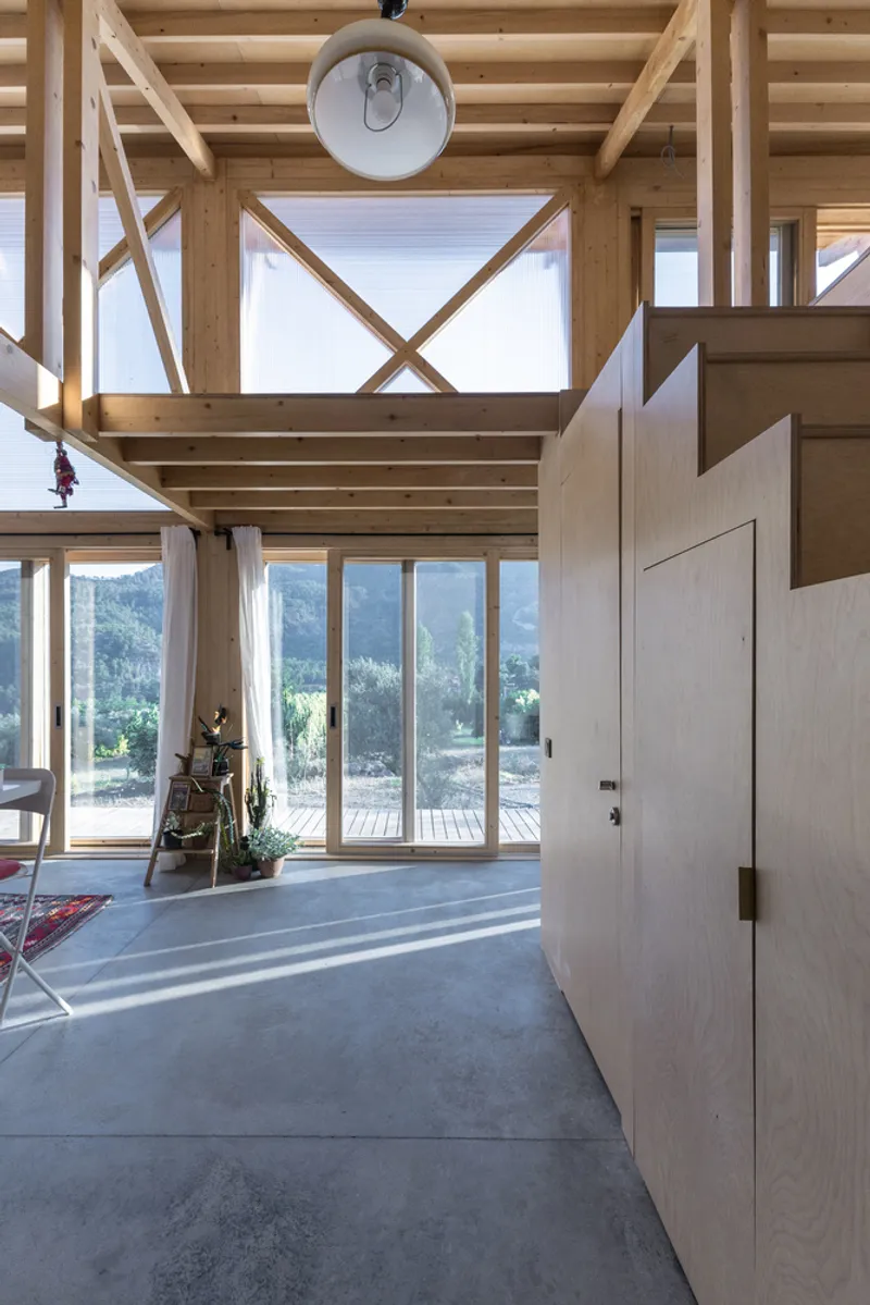 Entry hall with cross-braced timber frame casting shadows across concrete floor and white door