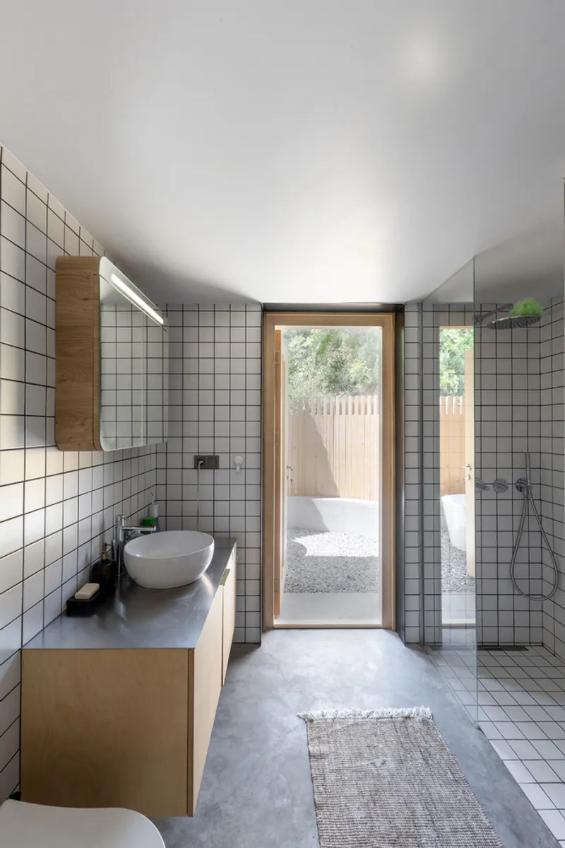 Bathroom with white grid tile walls and timber vanity leading to a gravel courtyard