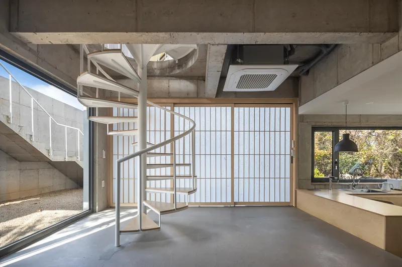 White spiral staircase and translucent sliding screen beside an open kitchen with exposed concrete ceiling