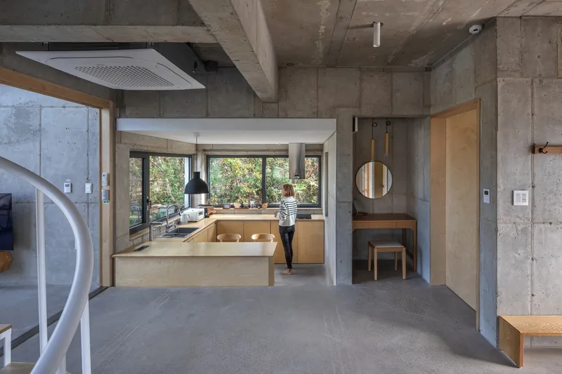 Open kitchen with timber cabinetry and person standing at window under exposed concrete slab