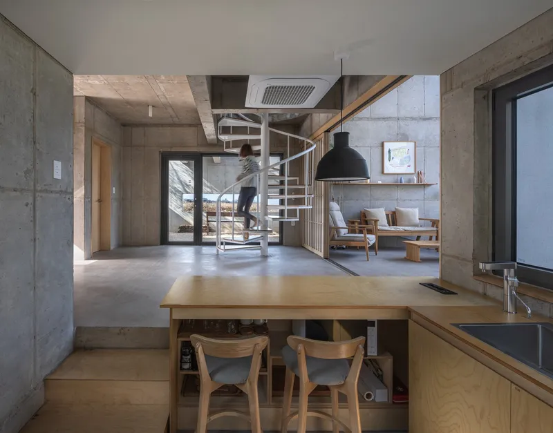 Open interior with exposed concrete walls and a white spiral staircase as a figure ascends