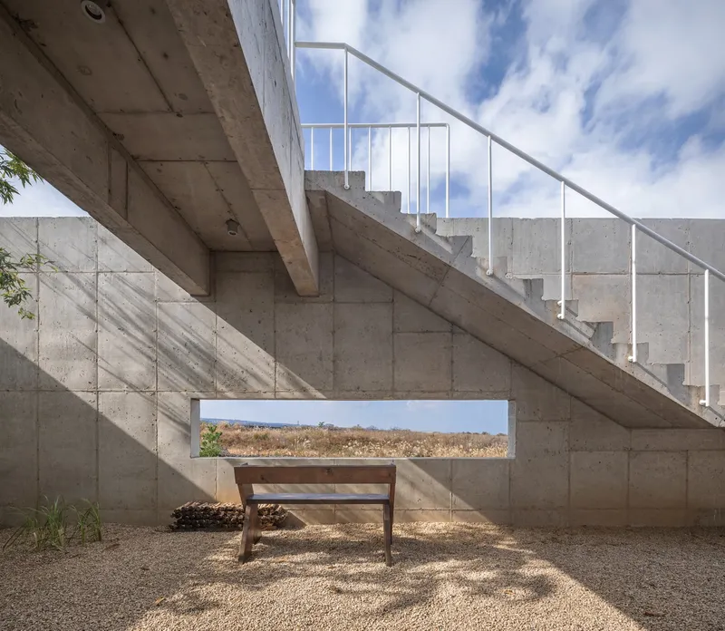 Exterior concrete staircase with metal railing ascending past a horizontal window slot framing the landscape