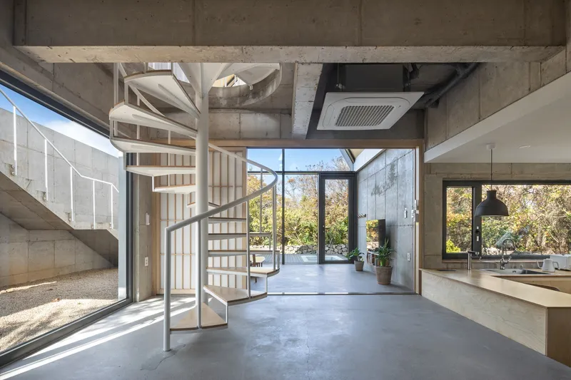 Interior double-height space with spiral staircase and exposed concrete ceiling opening to glazed terrace