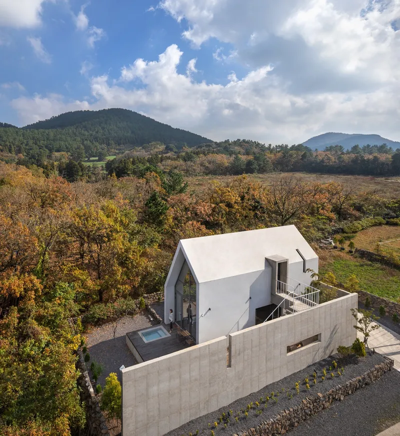 Aerial view of the gabled white volume and concrete courtyard wall amid autumn foliage and mountains