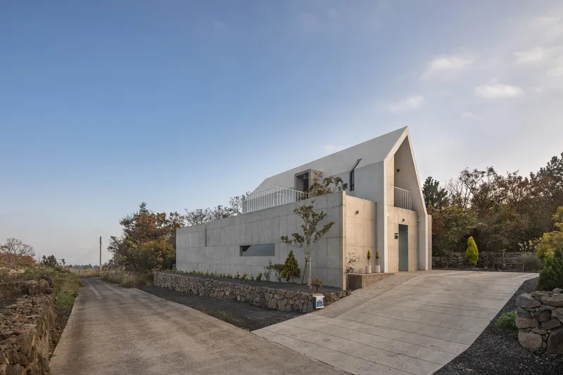 Curved concrete roof rising above board-formed walls along a sloping driveway at dusk