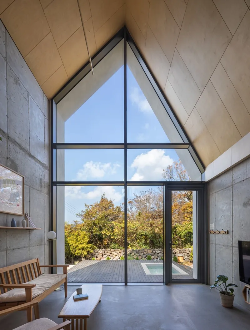 Double-height living space with triangular glazing framing deck and stone wall through black-framed doors