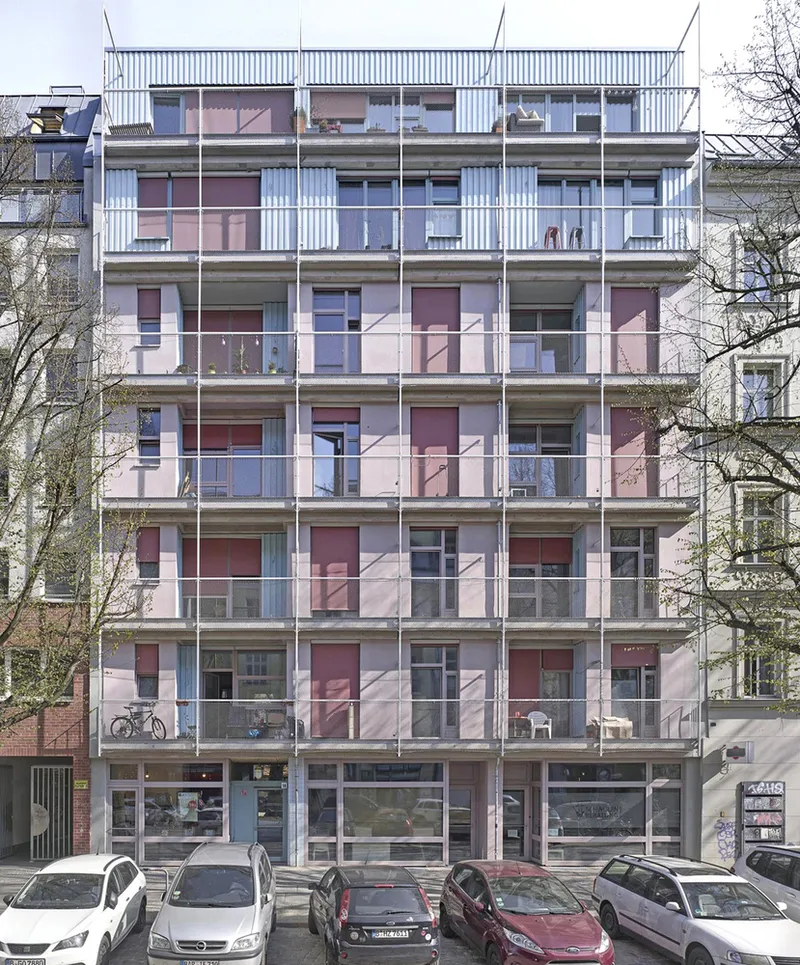 Street facade with pink and burgundy corrugated metal panels and recessed balconies flanked by bare trees