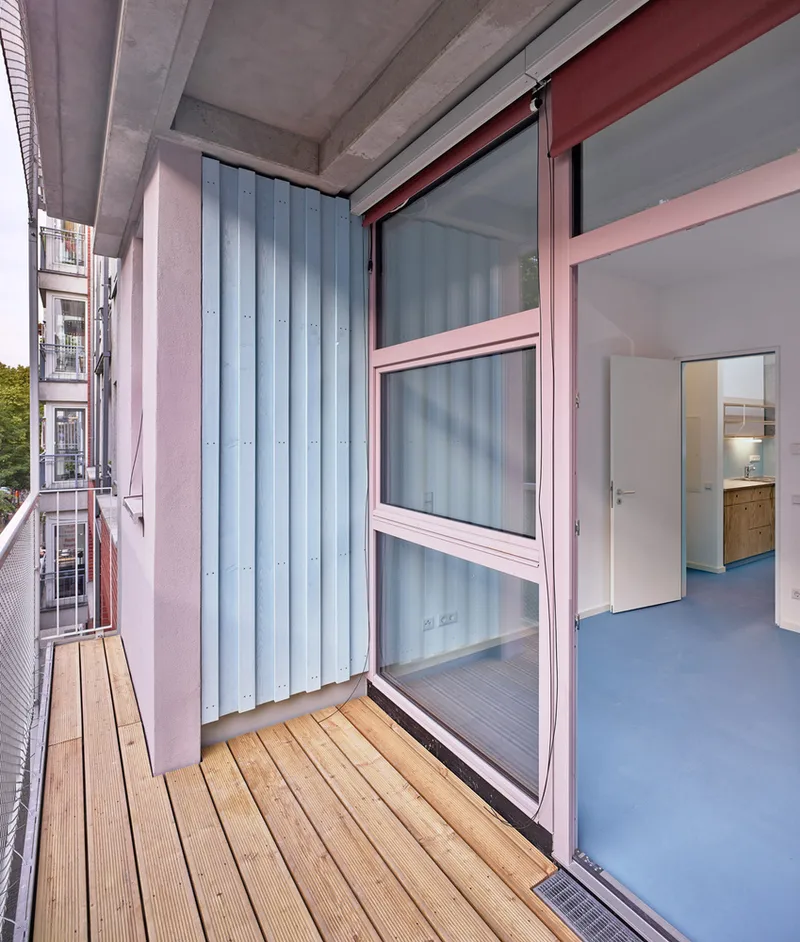 Balcony with timber decking, corrugated metal cladding, and sliding glass doors under exposed concrete soffit
