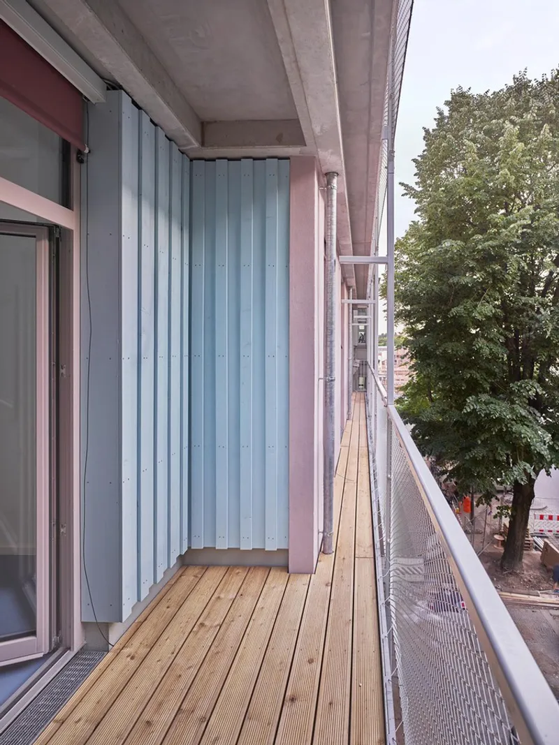 Timber-decked balcony with corrugated metal privacy screen, concrete soffit, and mesh railing overlooking trees