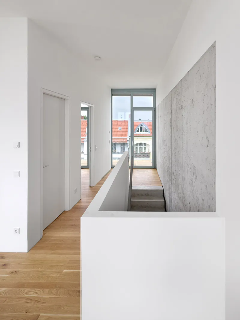 Upper hallway with oak flooring, concrete stairwell wall, and window framing view of neighboring rooftops