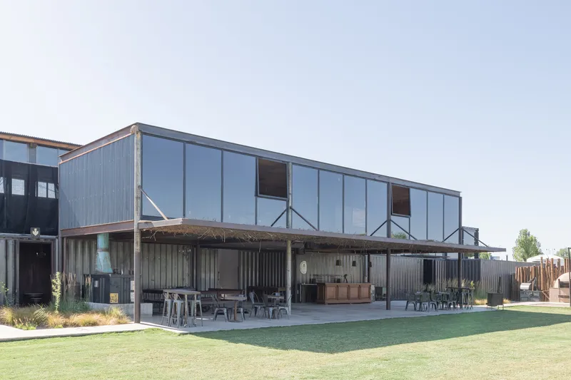 Covered outdoor terrace with corrugated metal screening, thatched roof shade and lawn in afternoon light