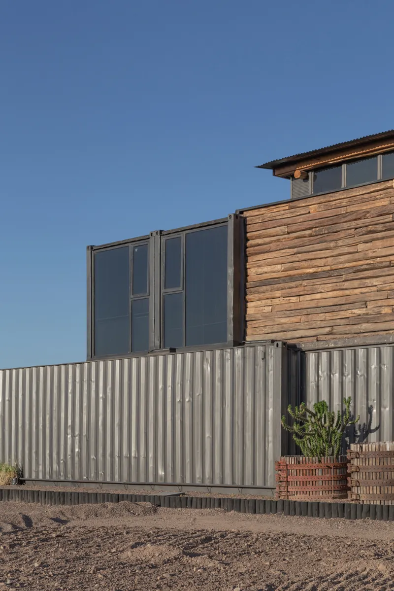 Corner detail showing corrugated metal base, timber siding and glazed upper volume under clear blue sky