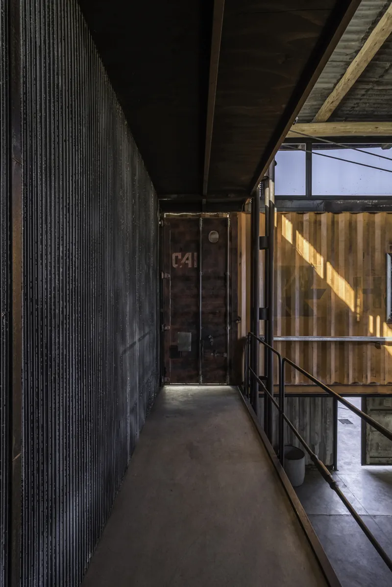 Narrow corridor with corrugated metal wall, weathered shipping container door and metal railing in afternoon light