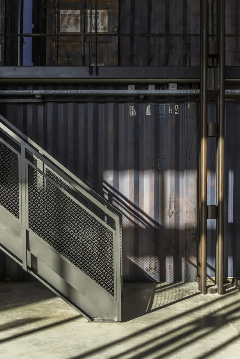 Metal stair with mesh infill panel beside corrugated shipping container volume casting angular shadows