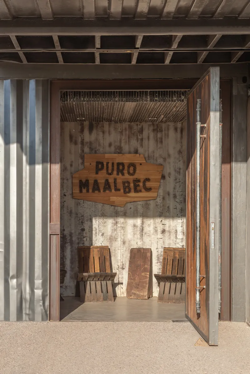 Tasting room entrance through corrugated metal walls with timber sign and slat installation above concrete floor