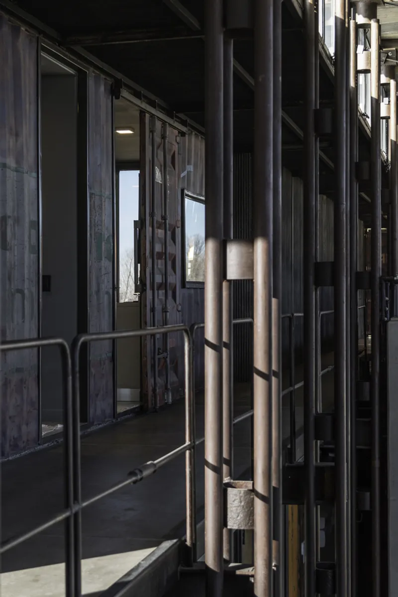 Exterior walkway with metal railing and dark weathered wood cladding in afternoon sunlight
