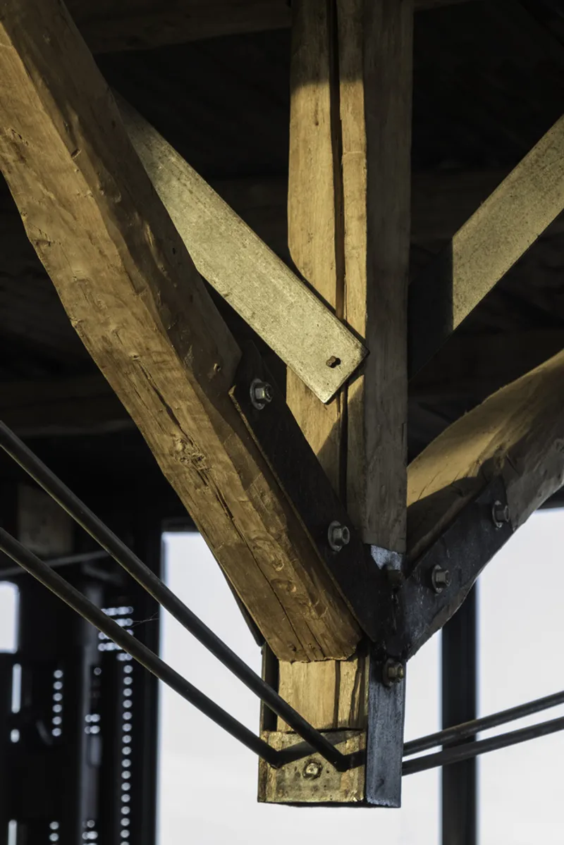 Close-up of bolted timber beam joint with diagonal bracing against black ceiling