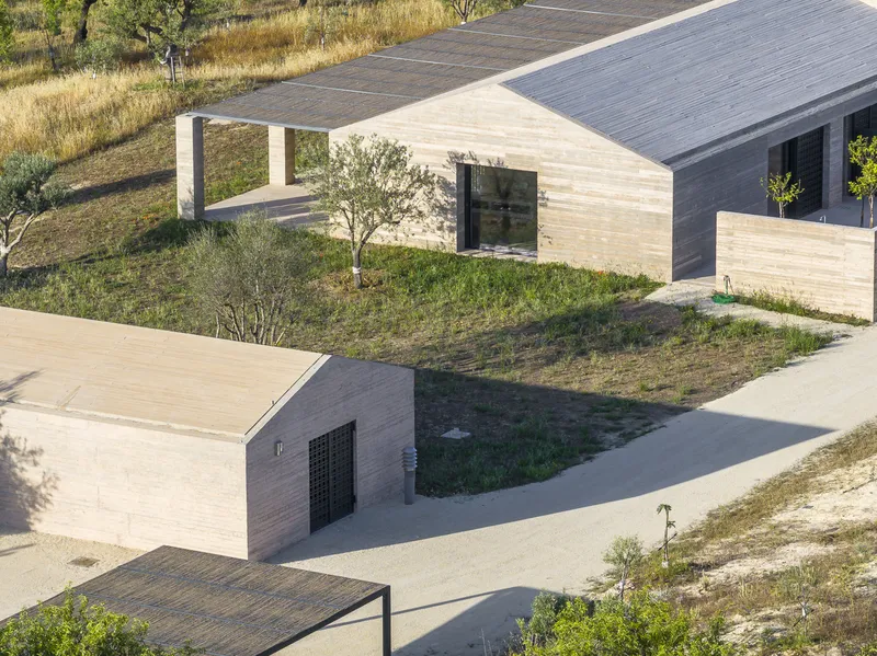 Aerial view of rammed earth volumes with gabled roofs set among grassy slopes and young trees