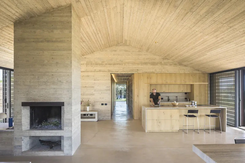 Open-plan living space with timber-lined vaulted ceiling, stone fireplace, and kitchen island with two occupants
