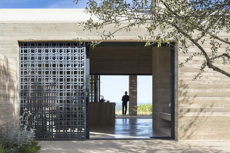 Threshold view through lattice screen and timber-clad opening with a figure silhouetted against the bright exterior