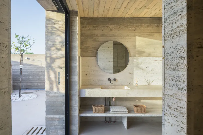 Bathroom vanity with round mirror and board-formed concrete walls adjacent to an exterior courtyard with a young tree