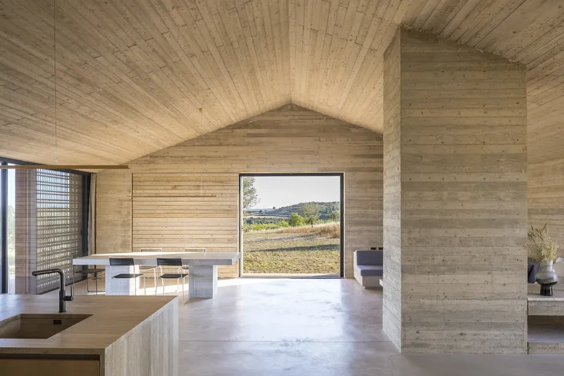 Open-plan living space with board-formed concrete walls and ceiling framing a landscape view through full-height glazing