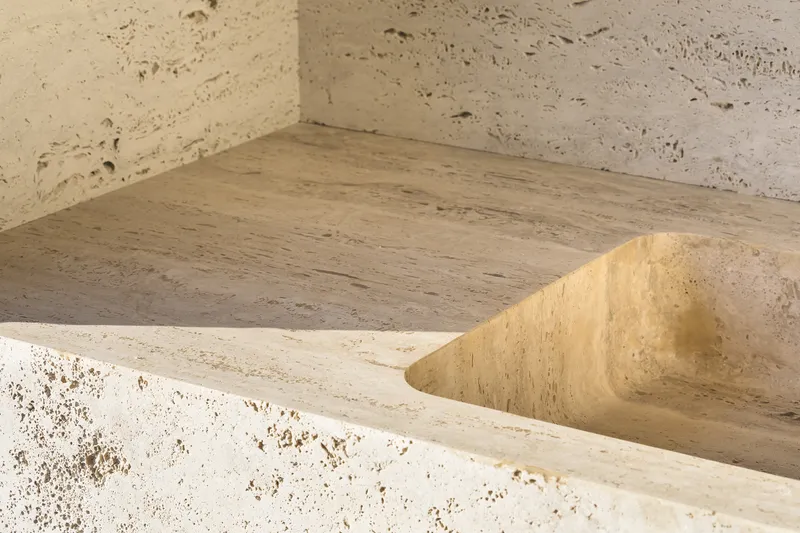 Close-up of board-formed concrete basin corner meeting porous stone walls in afternoon sunlight