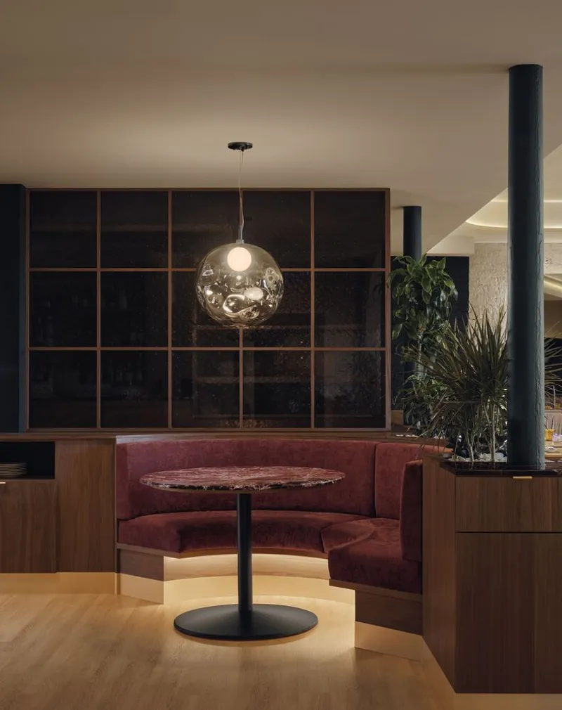 Curved banquette seating niche with spherical glass pendant and dark gridded wall behind potted plants