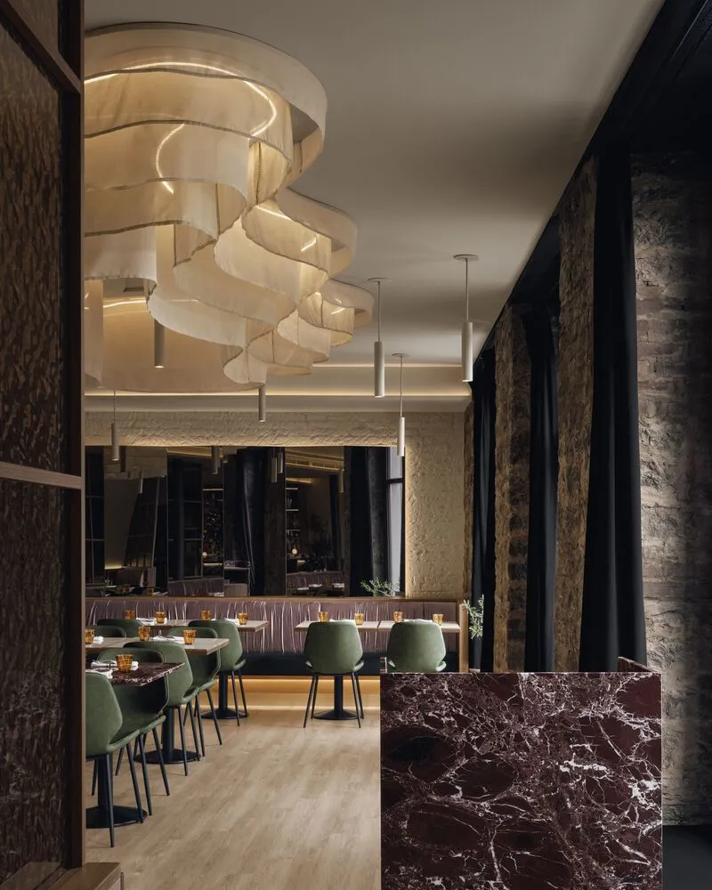 View toward the dining area showing layered sculptural lighting and a dark veined marble partition