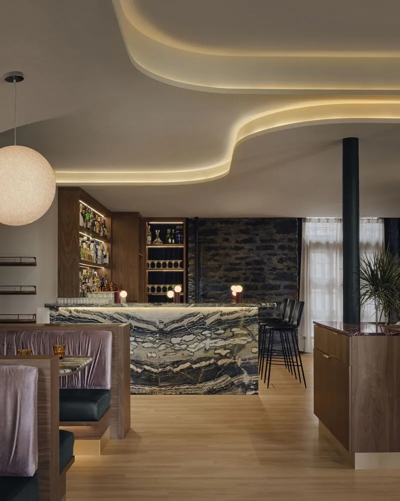 Bar counter clad in swirling black and cream marble below undulating cove-lit ceiling forms