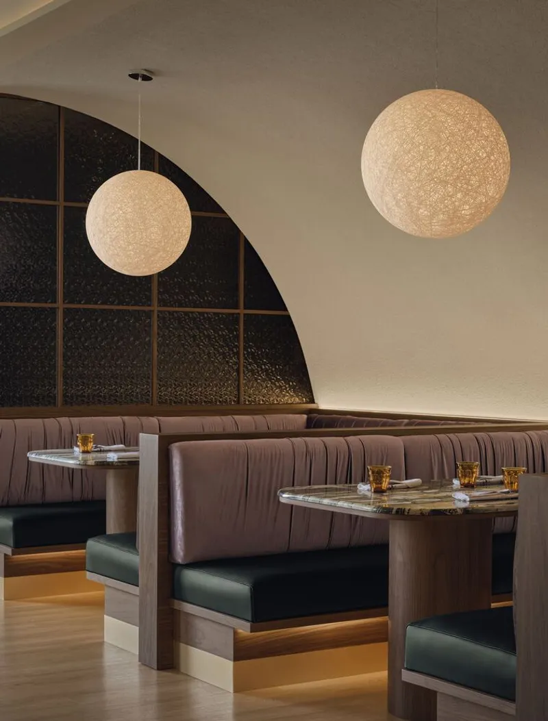 Booth seating with channeled upholstery below arched dark glass partition and two spherical pendant lights