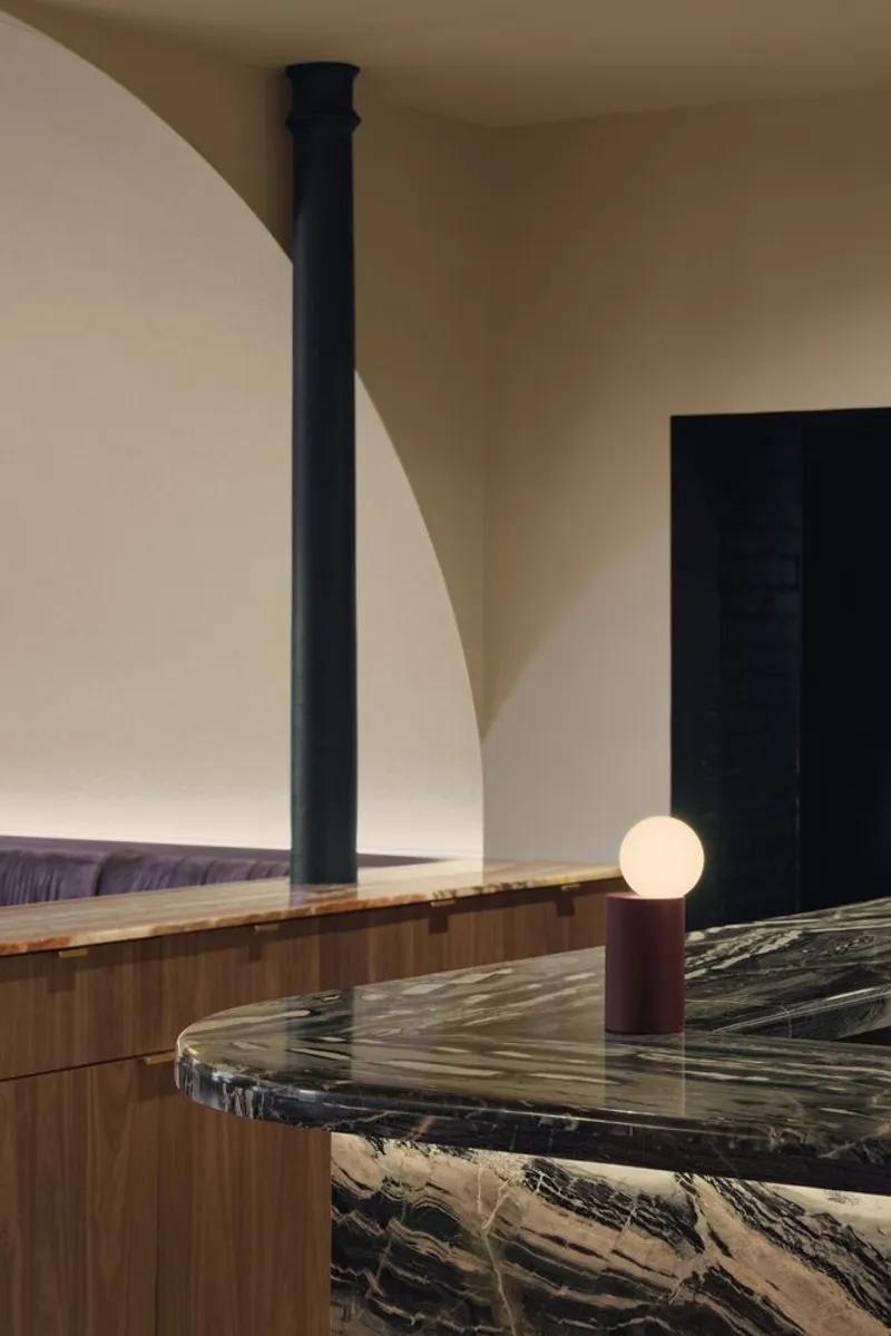 Black marble island counter with veined stone top and spherical table lamp under curved ceiling