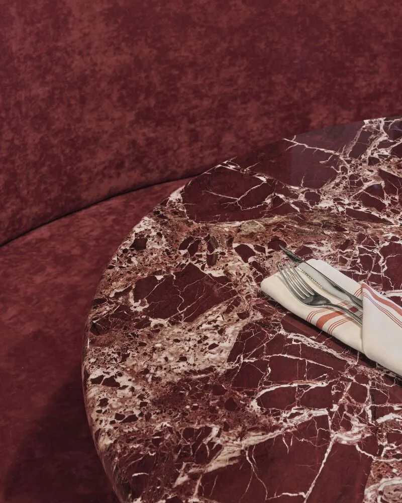 Red marble tabletop with white veining next to a burgundy upholstered banquette