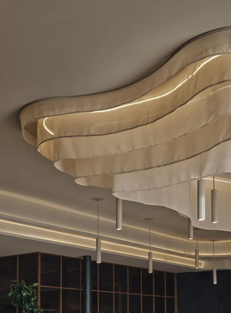 Layered fabric ceiling detail with integrated lighting and suspended cylindrical pendants below
