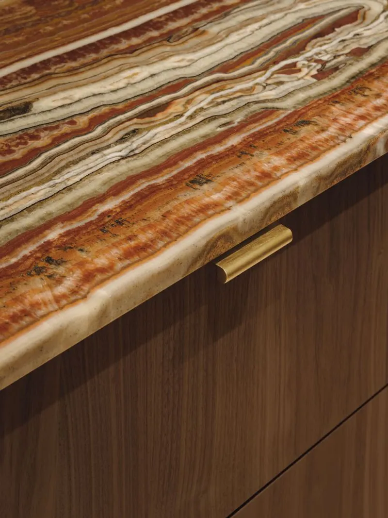 Striated onyx countertop edge with brass drawer pull against timber veneer cabinetry
