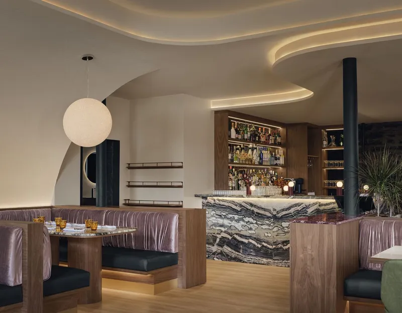 Bar counter clad in marbled stone with timber shelving and spherical pendant lamp
