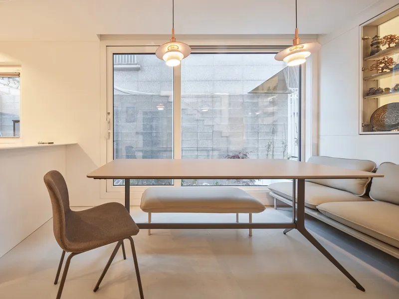 Dining area: white table with steel frame, bench seating and leather chair, two pendant lights, large window to side courtyard