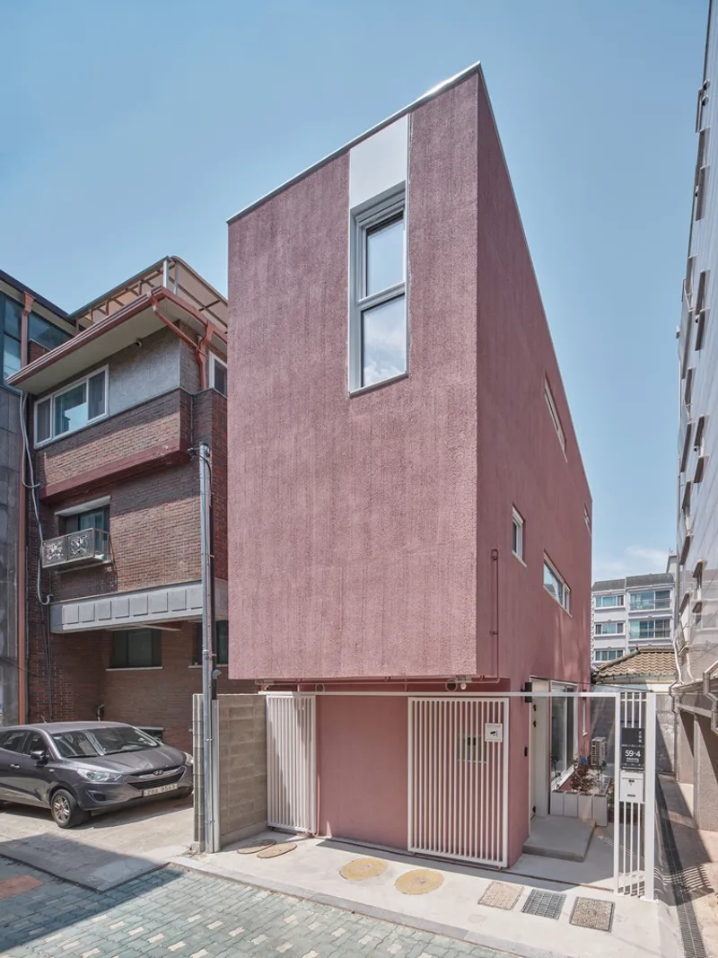 Front facade straight on: dusty pink tower, two narrow vertical windows, concrete base with garage, blue sky