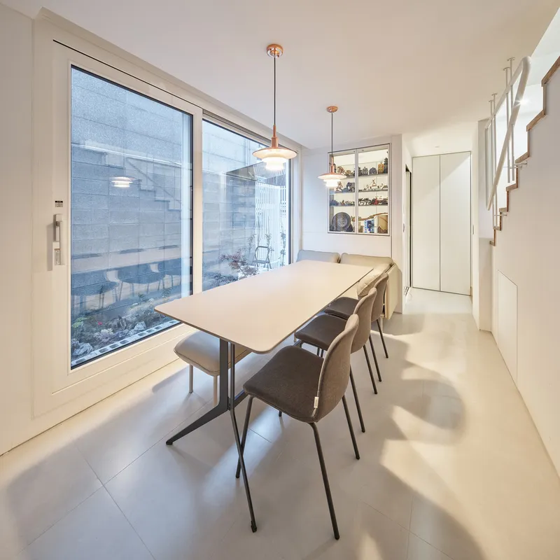 Dining room: white table, pendant lights, large sliding glass door to courtyard, staircase visible at right, light timber floor